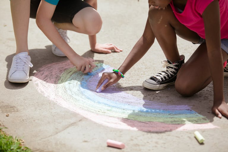 Fun summer activites for kids Kids having fun drawing a rainbow with chalk on the pavement in a park.